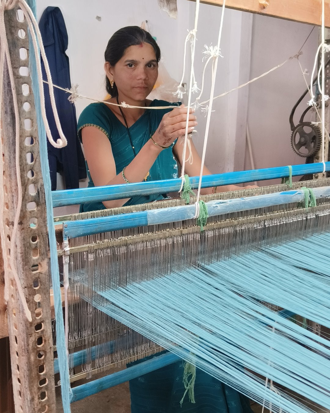 A weaver tying a sky-blue warp to the heddles while setting up her loom