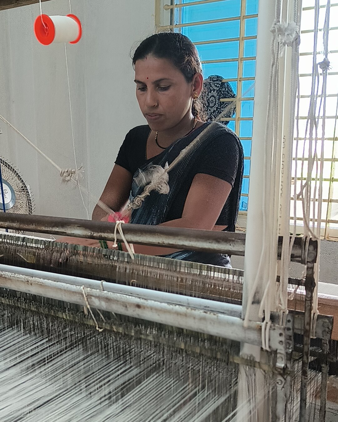 A weaver working the shuttle across an ivory cotton warp