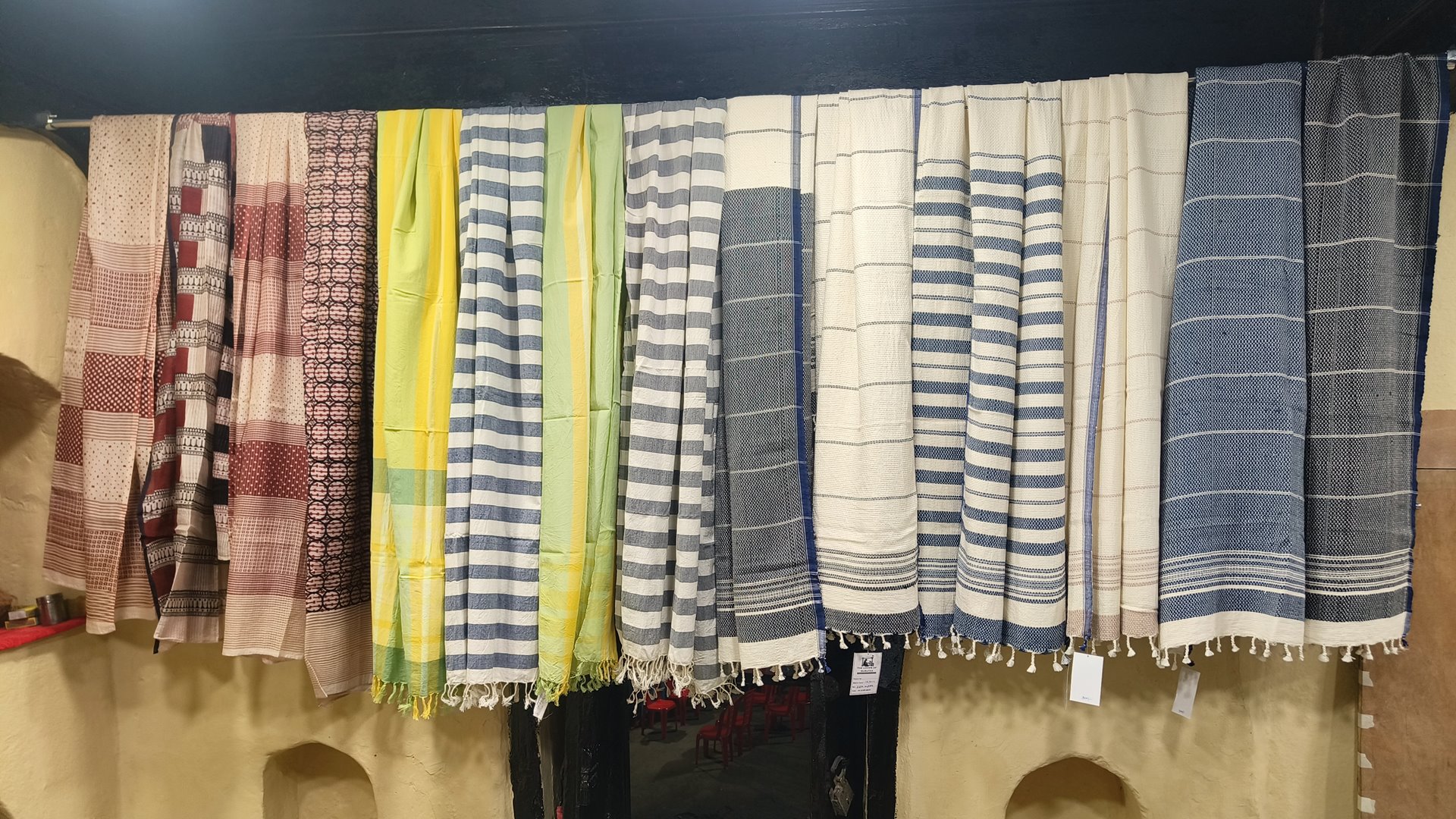 Handwoven cotton stoles in striped and patterned weaves hanging in a row